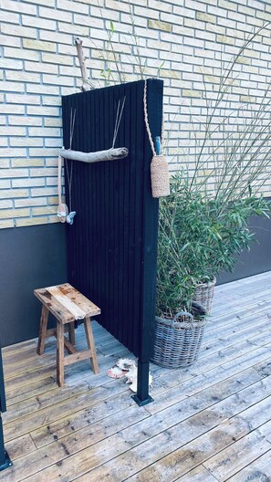 A wooden stool, a black partition, a woven basket, and a potted plant on a wooden deck. - Cottage with 400 m to the water and the marina (Østerby Havn)