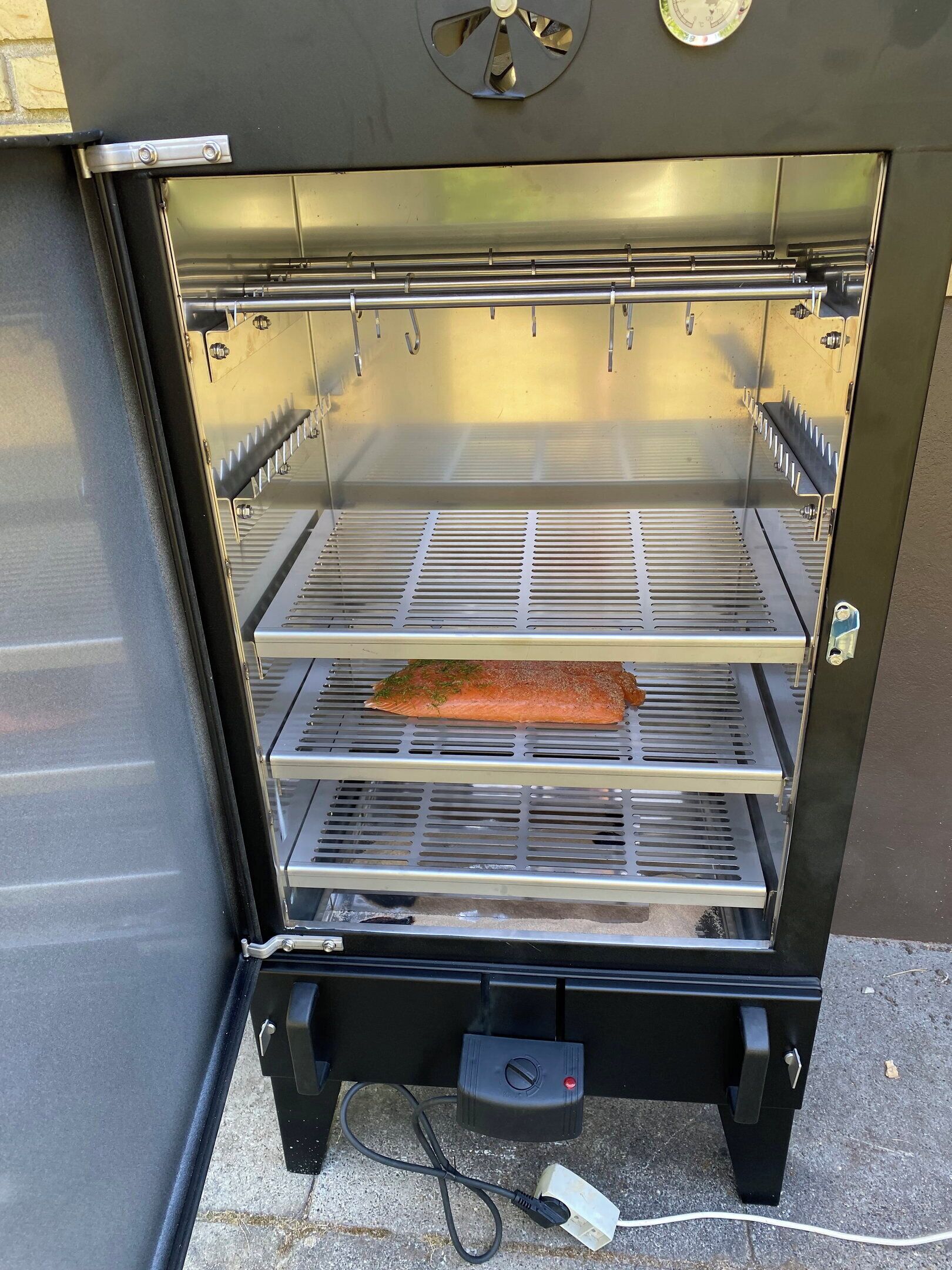 Een buitenbarbecue met een rooster, een snoer en een bedieningspaneel.