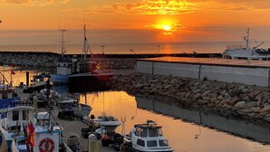 A marina with boats docked, a rocky breakwater, and a sunset over the water.