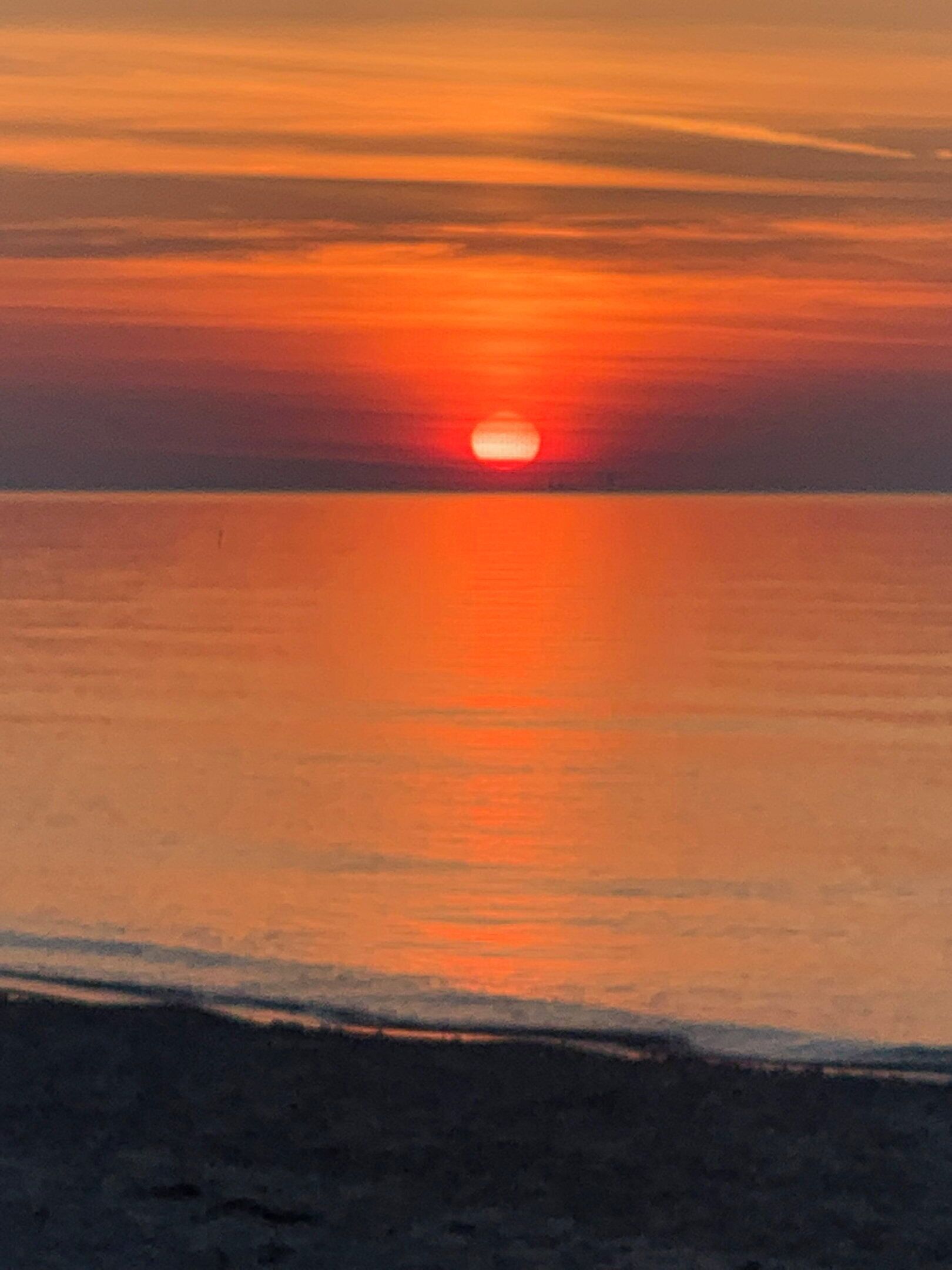 En solnedgång över ett stilla hav, med en strand i förgrunden.