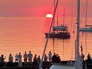 Een zonsondergang boven een rustig wateroppervlak met mensen op een steiger.