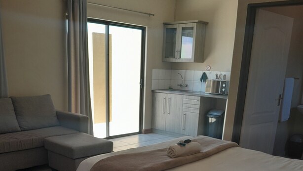 A hotel room with a large bed, a sofa, a kitchenette, and a sliding glass door to the outside. - High Breeze Lodge (Upington)