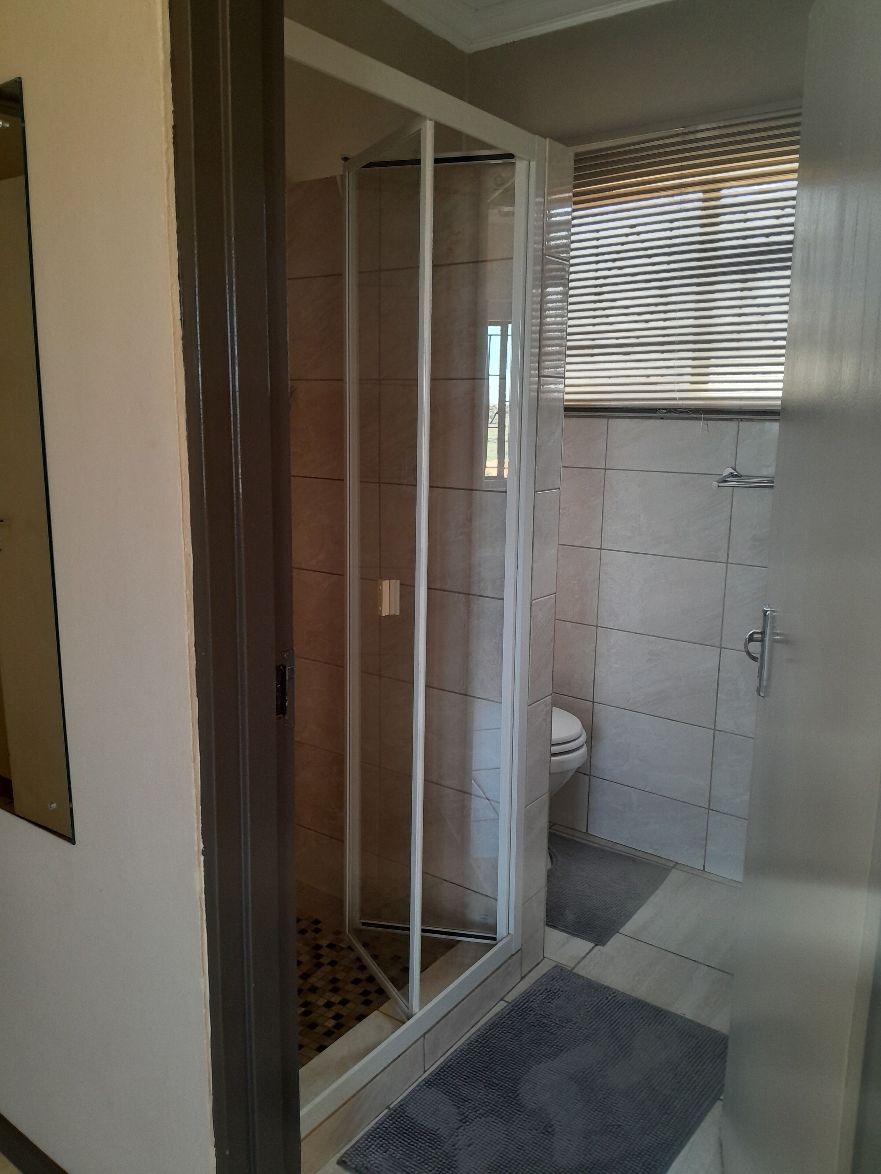 Une salle de bain avec une douche à parois de verre, des toilettes et une fenêtre avec des stores.