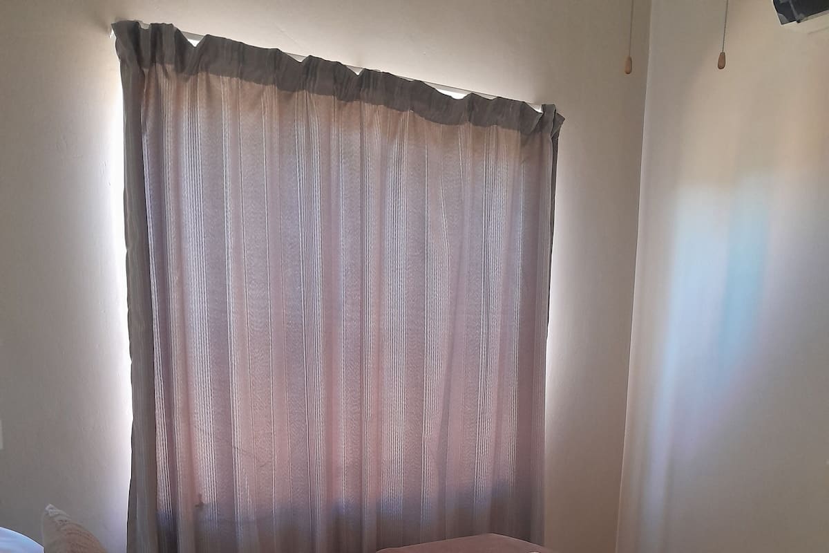 A neatly made bed with a white duvet, a brown throw blanket, and a rolled-up towel.