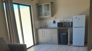 A modern living room with a sofa and ottoman, a kitchen with a refrigerator, microwave, and cabinets, and a sliding glass door to the outside. - High Breeze Lodge (Upington)