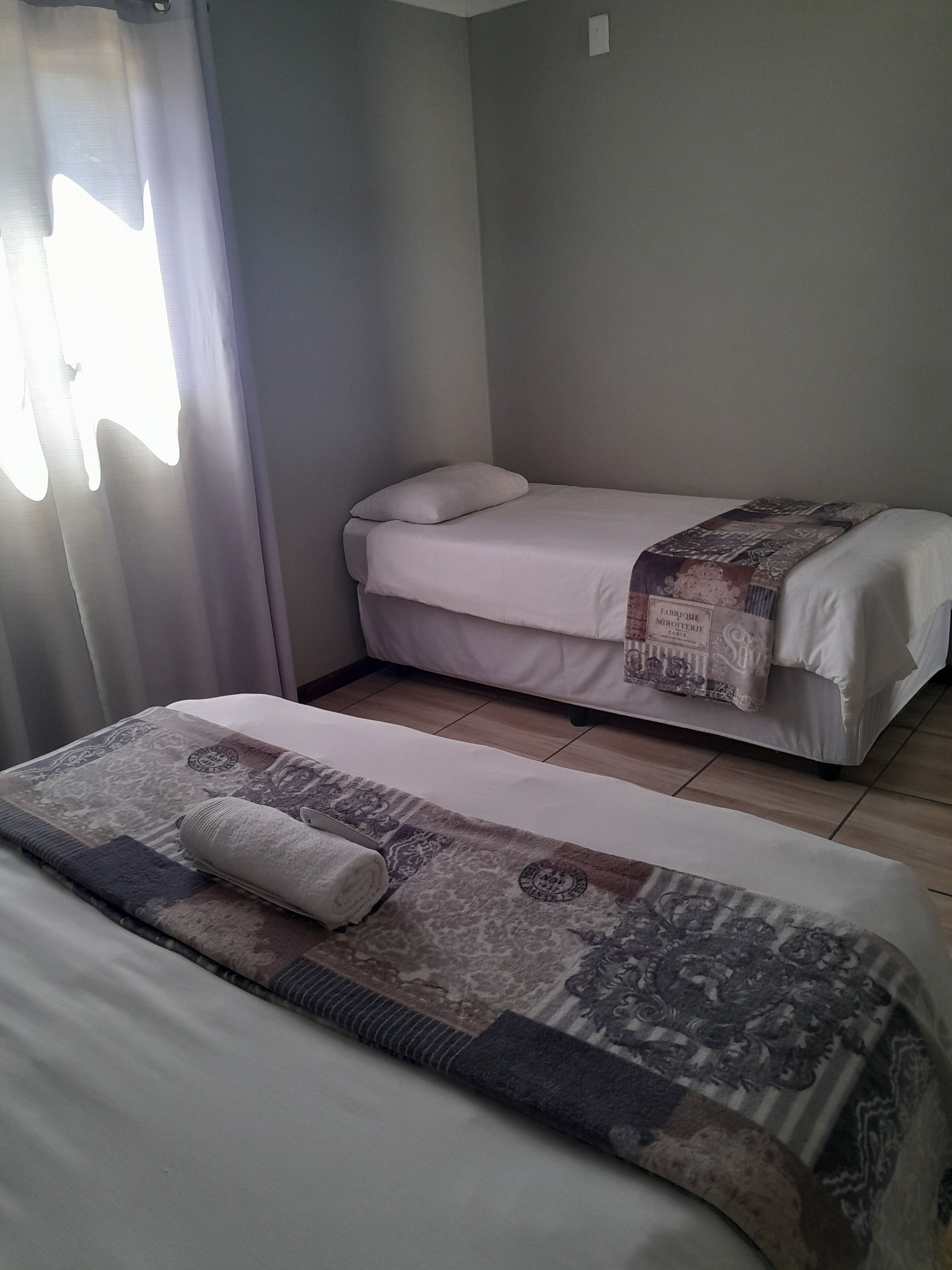 Habitación de hotel con dos camas individuales, una con una colcha estampada y la otra con una colcha blanca lisa.