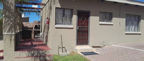 Un edificio de dos pisos con una puerta roja, un extintor y un pequeño jardín.
