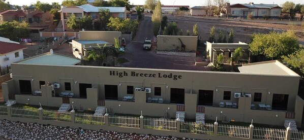 Rakennuksessa on kyltti, jossa lukee ”High Breeze Lodge”, ja siinä on useita huoneita, aidattu pysäköintialue sekä näkymä ympäröiviin taloihin.
