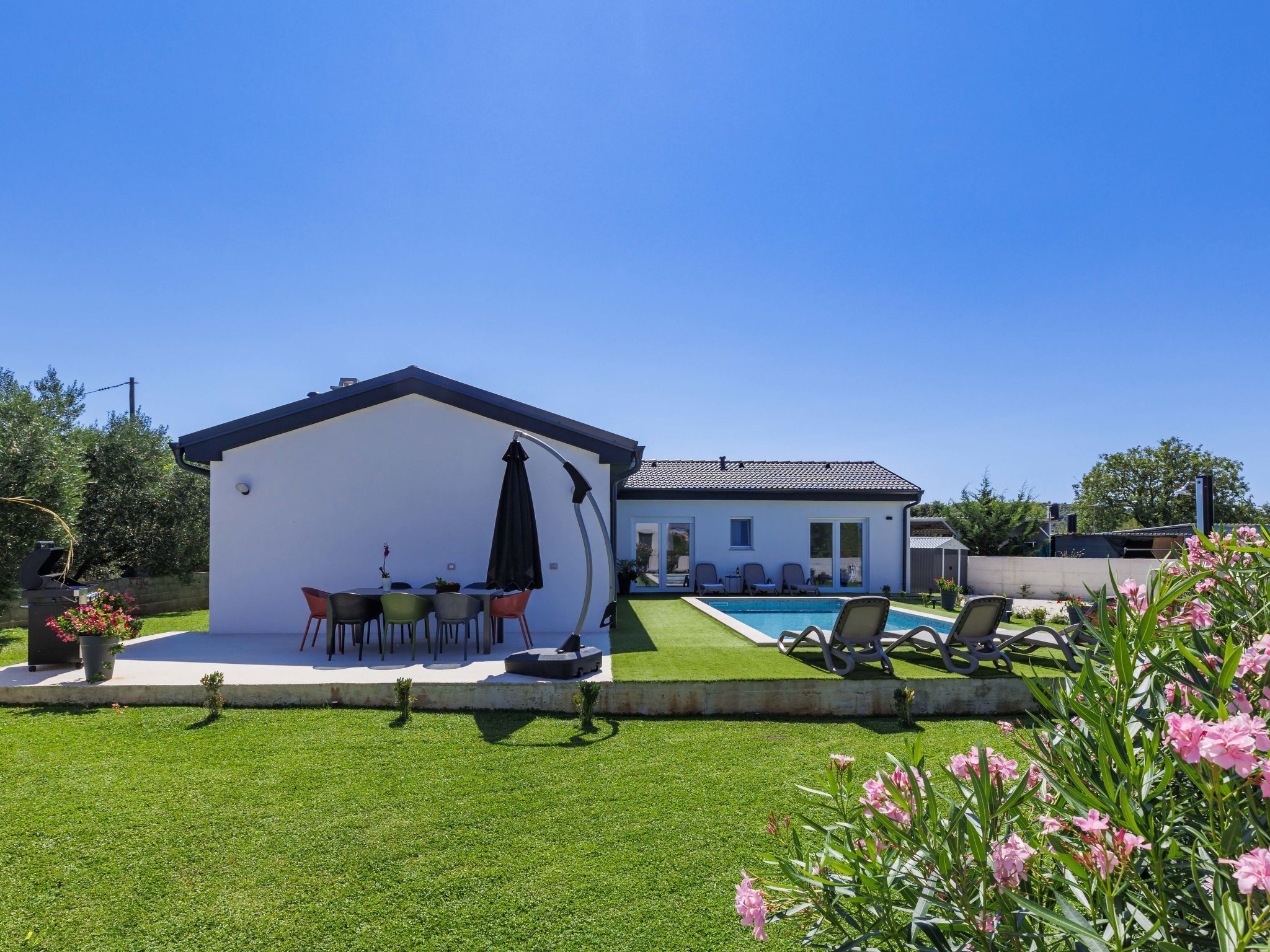 Ein modernes Haus mit überdachter Terrasse, Schwimmbad und gepflegtem Rasen.