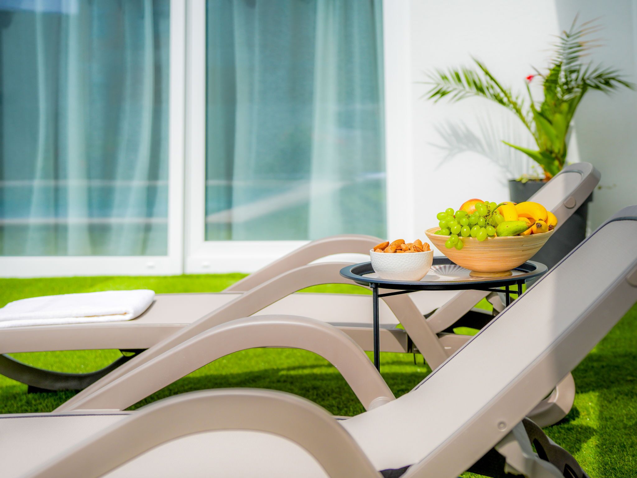 Un área de descanso con dos sillones blancos, una mesita baja con un tazón de frutas y nueces, y una planta en maceta.