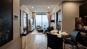 Une chambre d’hôtel moderne dotée d’un coin repas, d’un canapé, d’une télévision et d’une grande fenêtre avec des rideaux.