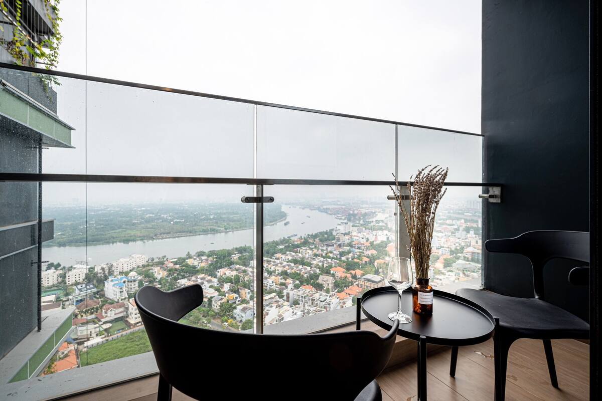 A balcony with a view of a river and cityscape, featuring a table with a vase and chairs.