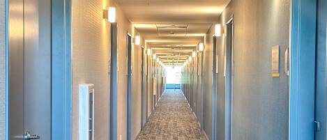 A hotel hallway with carpeted floors, doors on both sides, and overhead lighting.