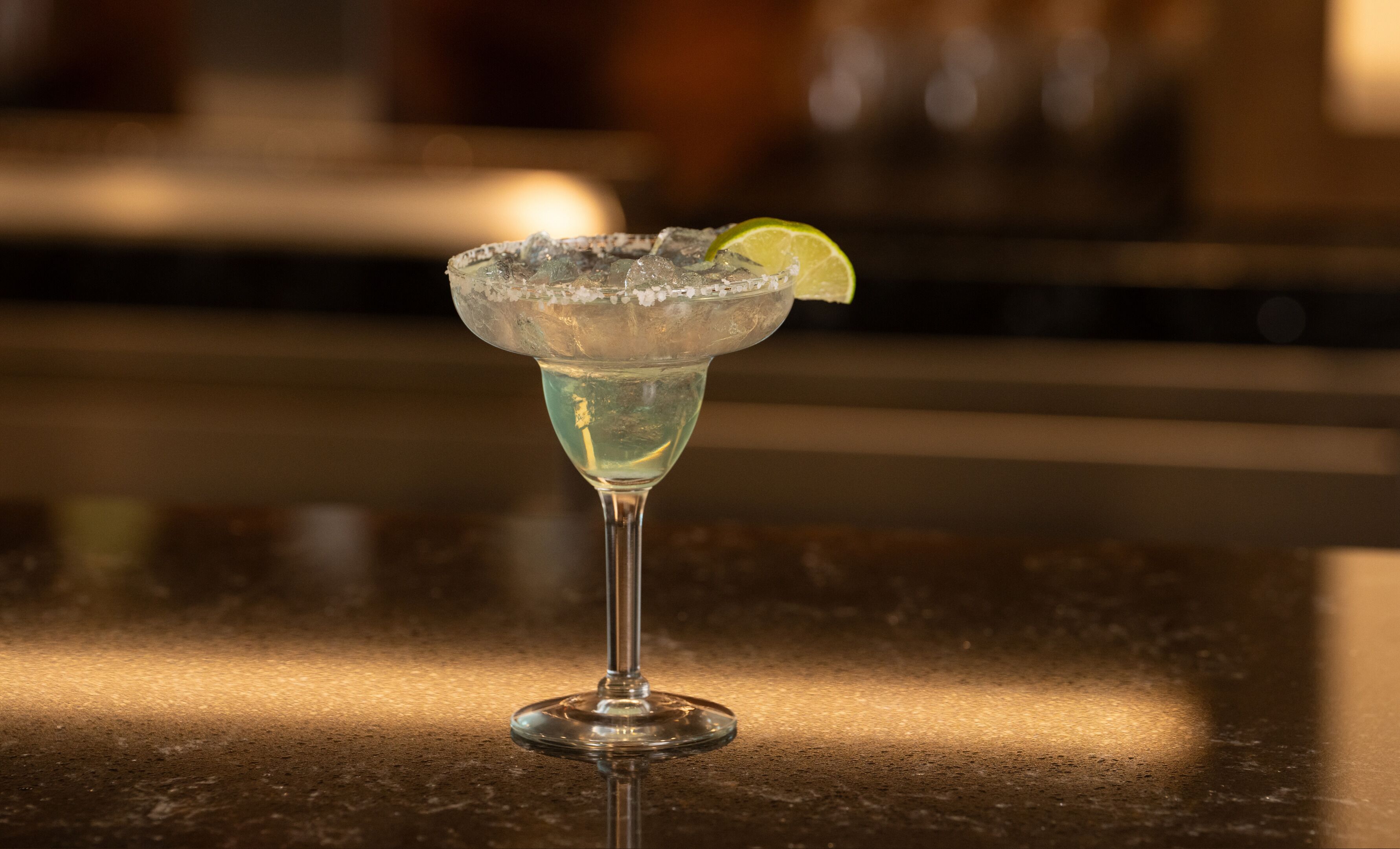 A cocktail glass with ice and a lime slice on a bar counter.