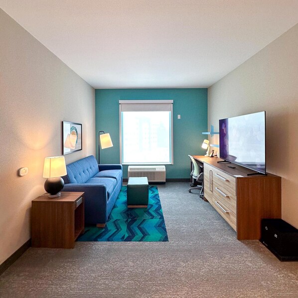 Habitación de hotel compacta con un sofá azul, un escritorio pequeño, televisión y ventana con vistas.