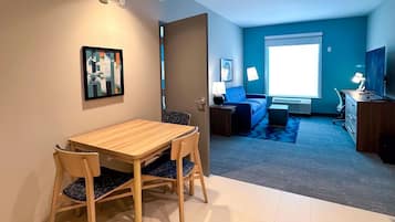 A modern living room with a blue sofa, a coffee table, and a TV. There's a dining area with a wooden table and chairs.
