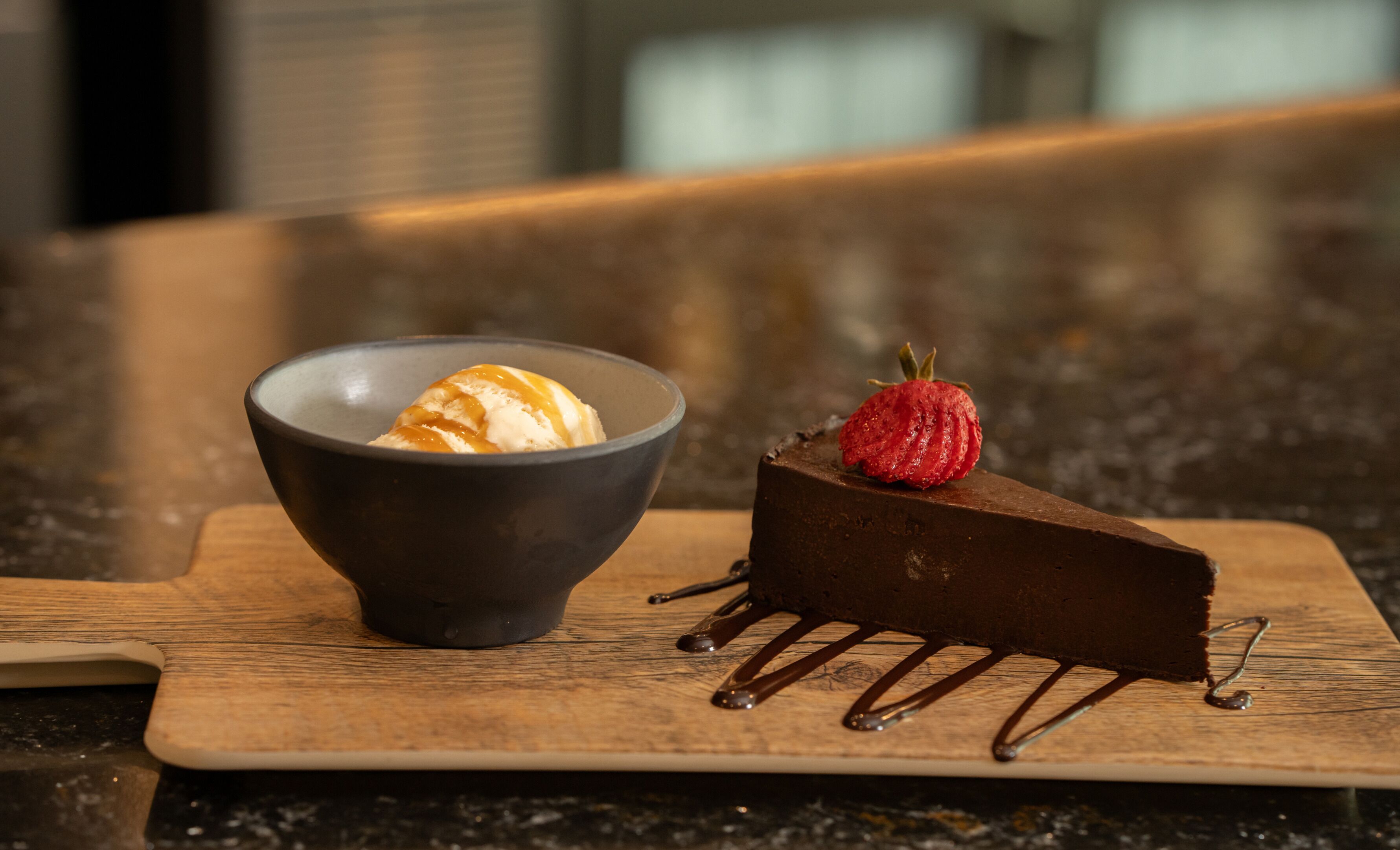Un postre con un trozo de chocolate y un bol de helado sobre una tabla de madera.