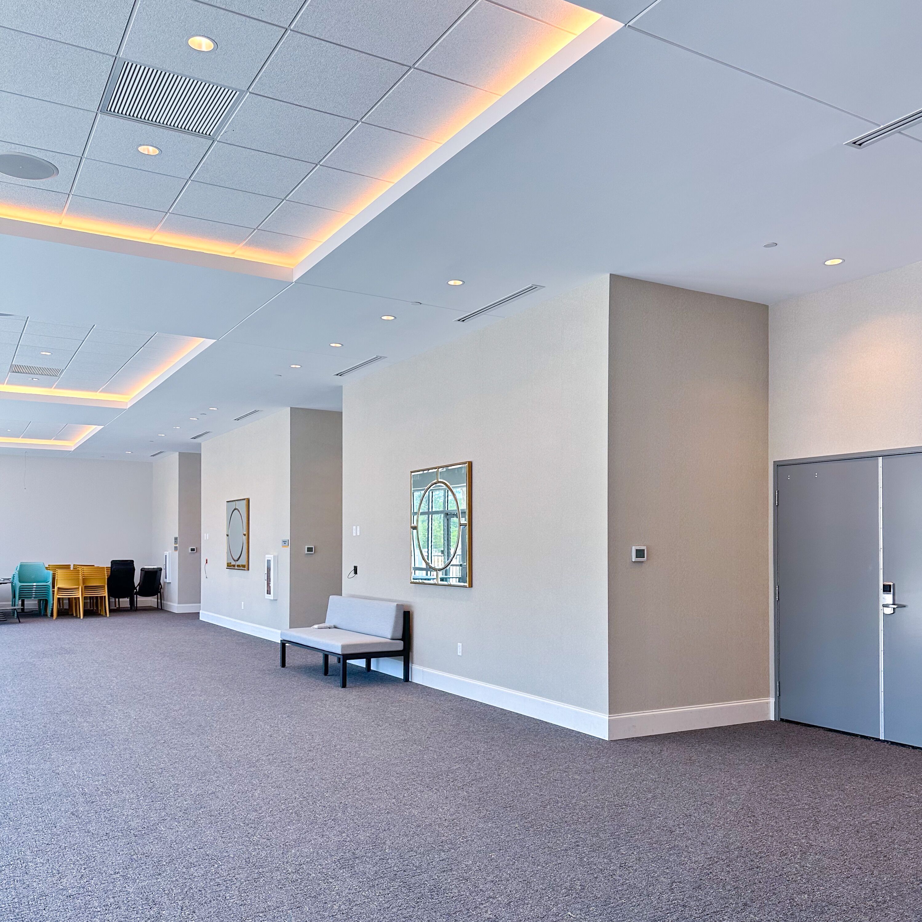 A spacious lobby with a high ceiling, recessed lighting, a seating area, and a door on the right.