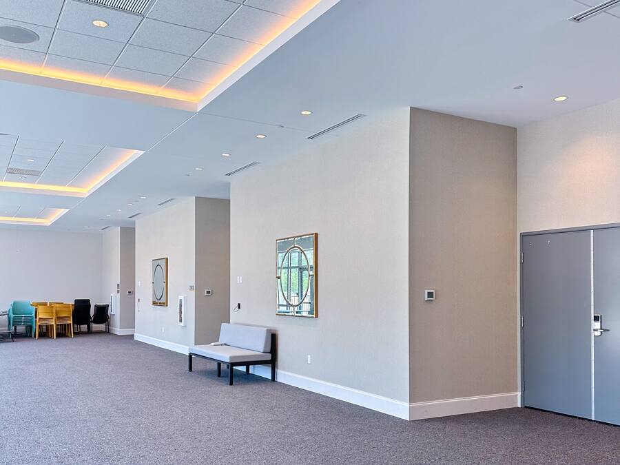 A spacious lobby with a high ceiling, recessed lighting, a seating area, and a door on the right.