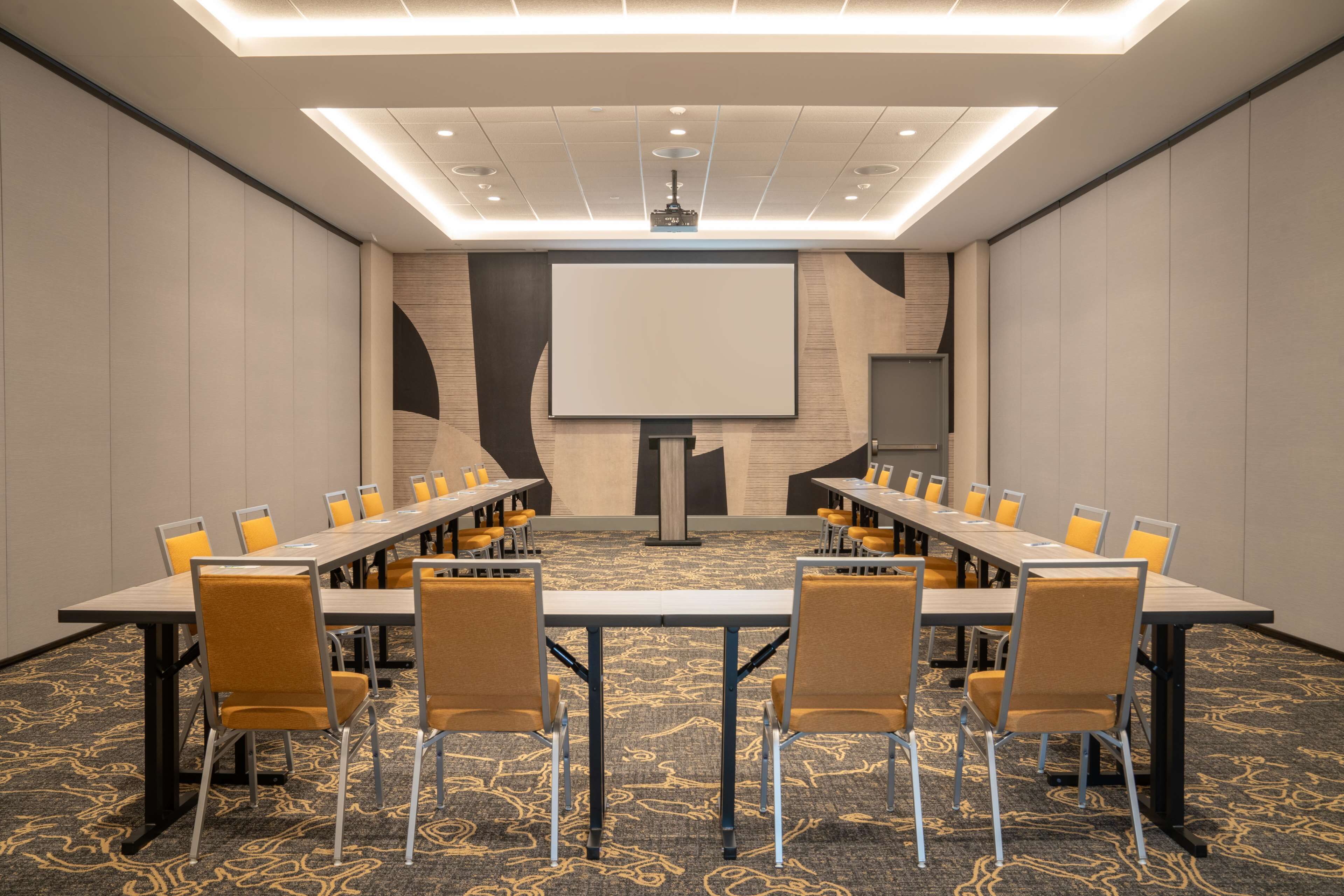 Una sala conferenze con un lungo tavolo, sedie, uno schermo per proiettore e pavimento rivestito di moquette.