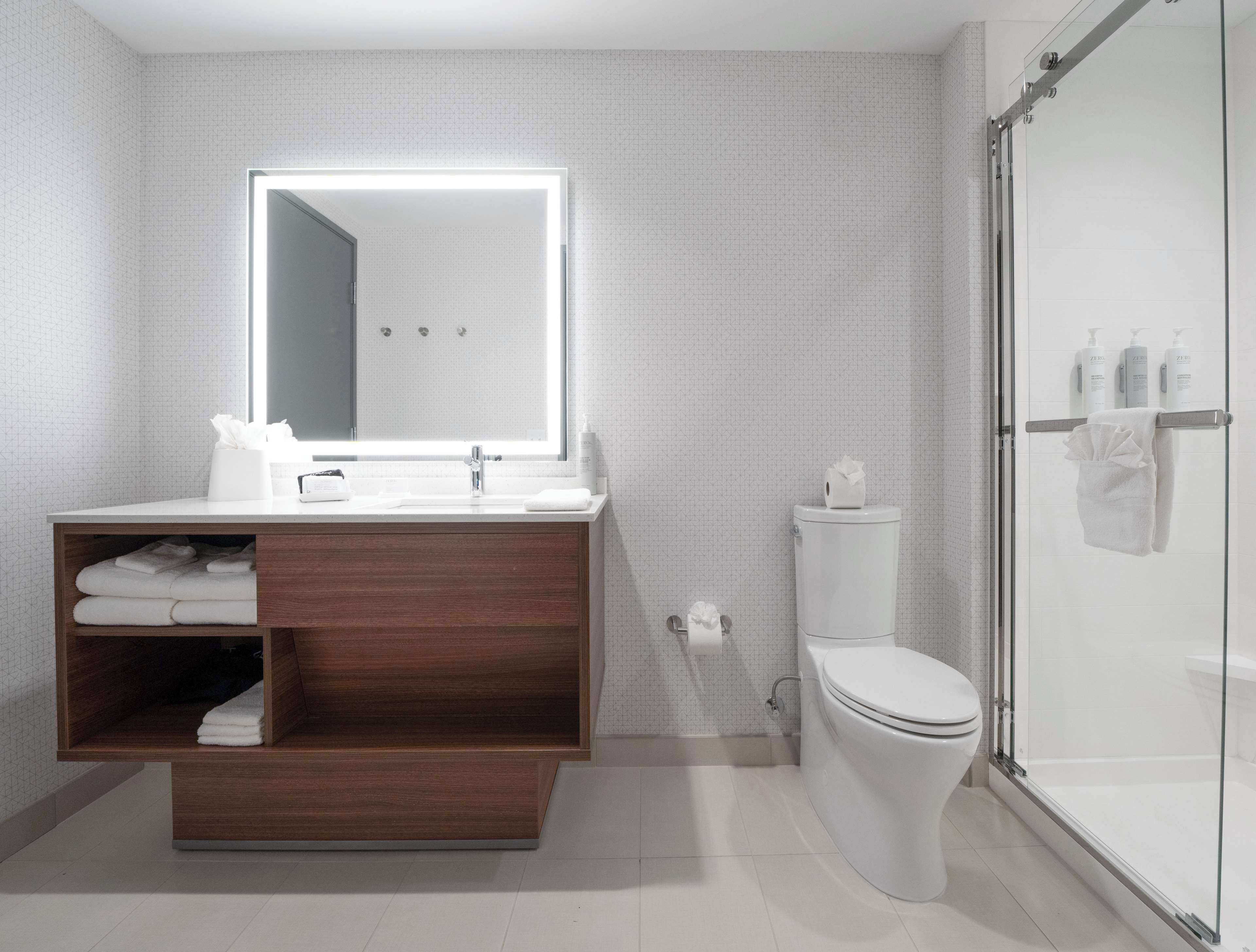 Un baño moderno con tocador de madera, un espejo grande, inodoro y cabina de ducha de vidrio.