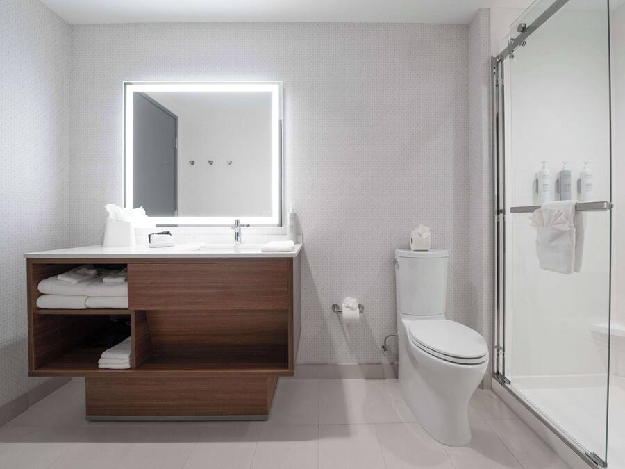 Un baño moderno con tocador de madera, un espejo grande, inodoro y cabina de ducha de vidrio.