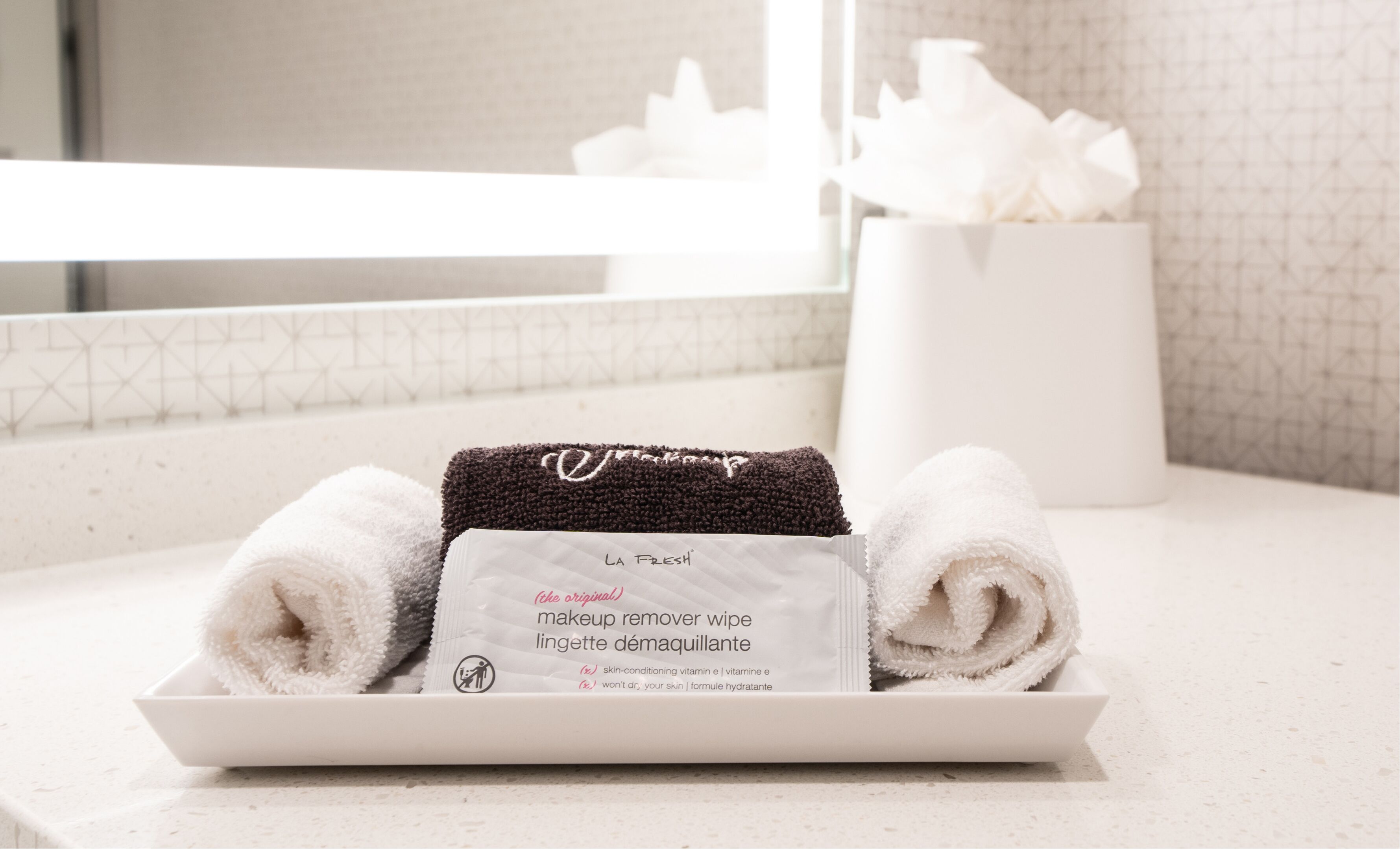 A tray with two towels and a makeup remover wipe on a bathroom counter.
