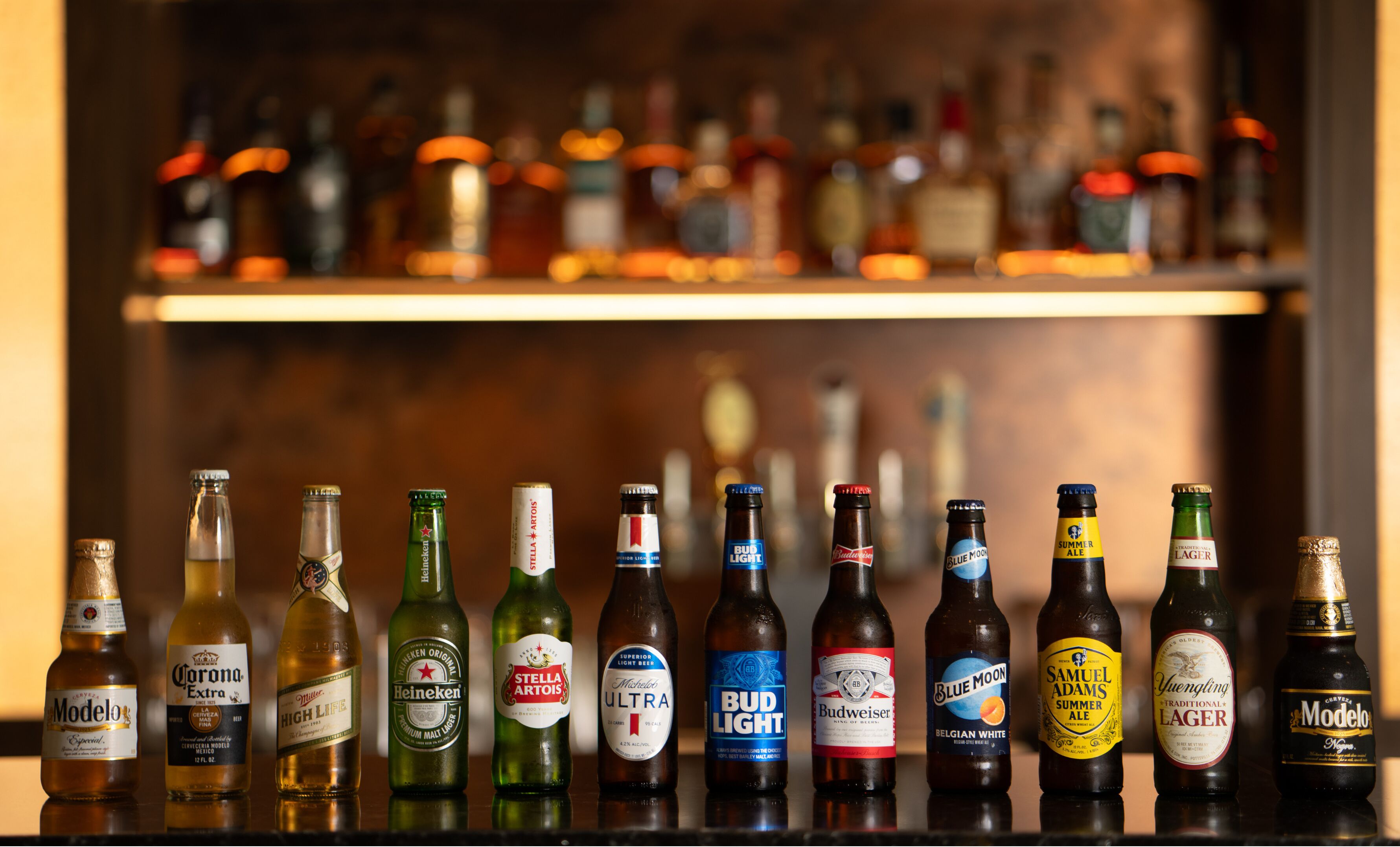 A selection of beer bottles on a bar counter with a blurred background of shelves filled with various bottles.