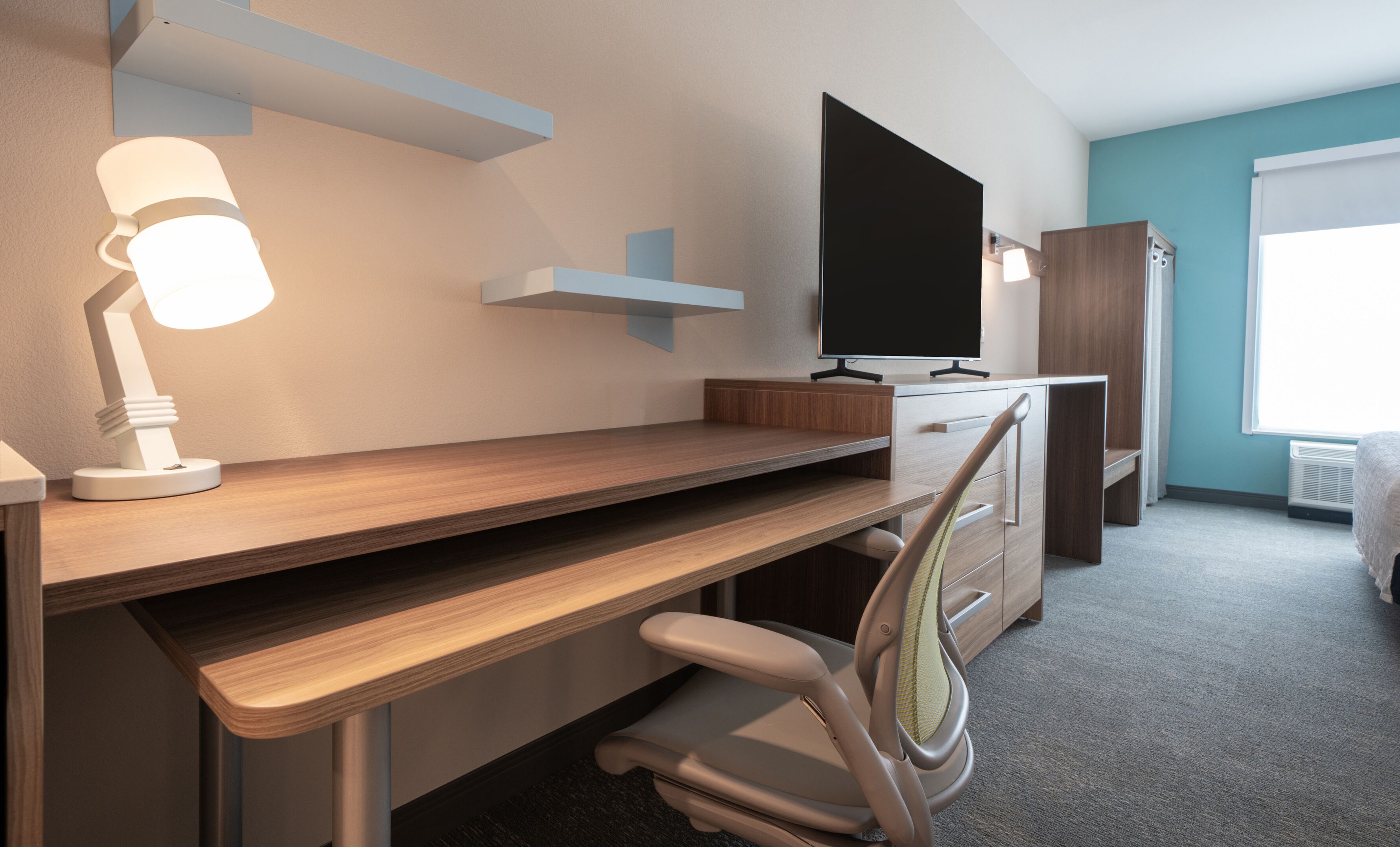 A modern office space with a desk, chair, TV, and storage cabinets.