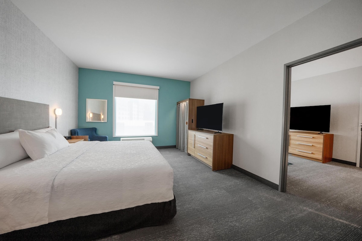 Una habitación de hotel moderna con una cama grande, un televisor, un mueble de madera y un espejo.