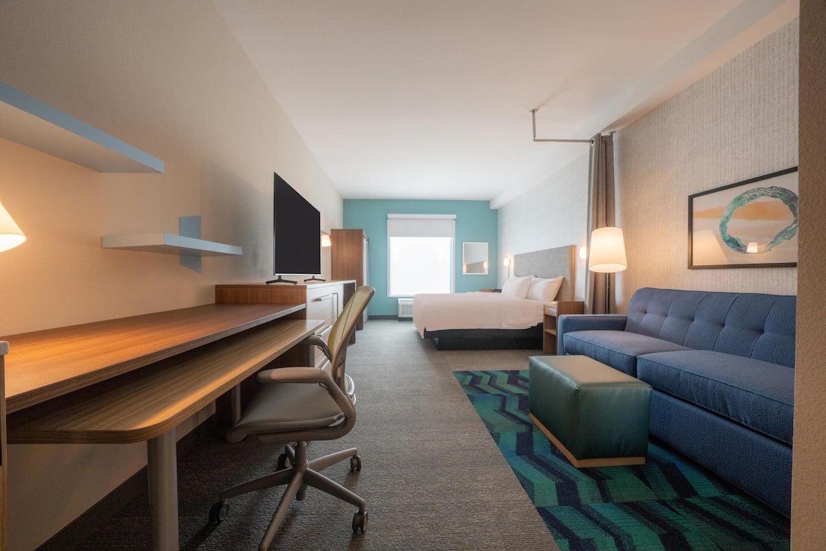 Habitación de hotel con escritorio, silla de oficina, cama, sofá y televisor.
