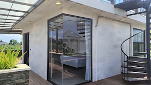 A modern outdoor living space with a glass door leading to a balcony, a wooden deck, and a staircase. - Ocean view 2-bedrooms Yudistira villa 50m from the beach (Bali)