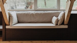 Un espacio tipo loft con vigas de madera a la vista, un banco empotrado con cojines, ventanas amplias y vistas al exterior.