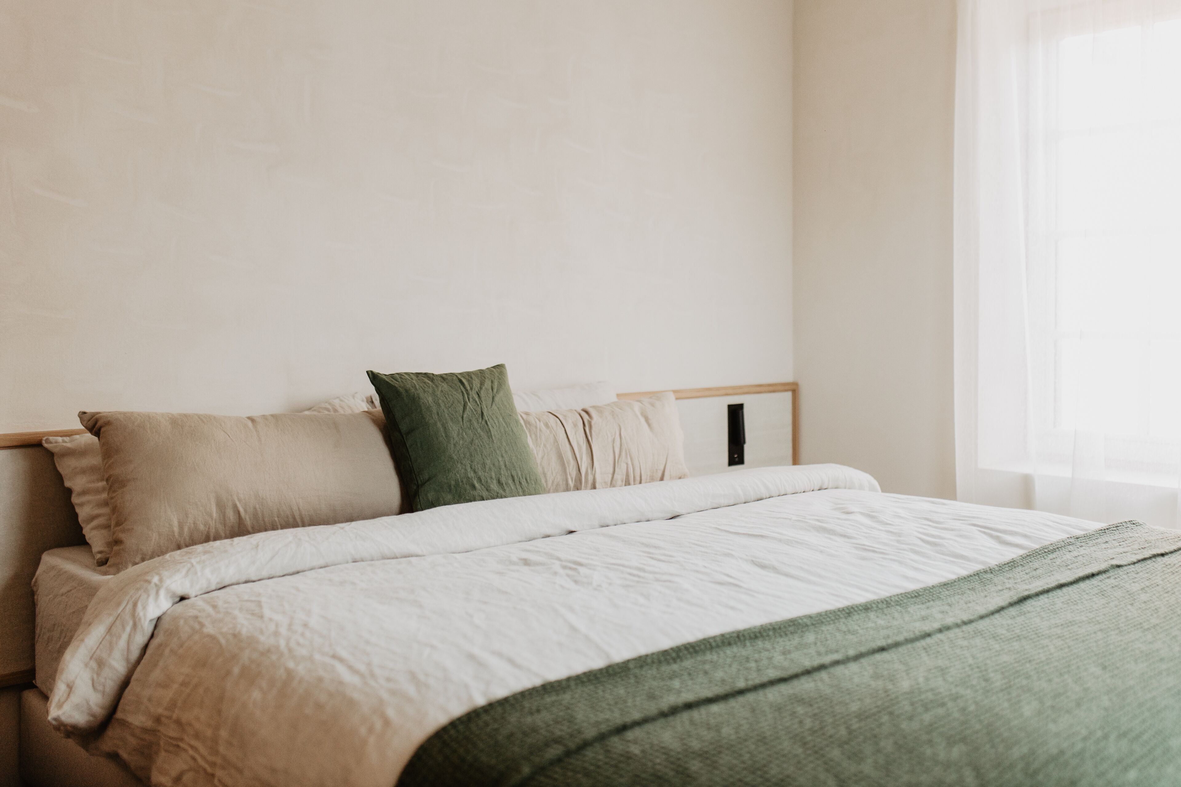 Una cama bien hecha con una manta verde, un cabecero de madera y una pared lisa.