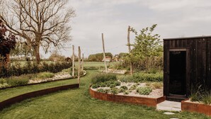Un jardín ajardinado con una estructura de madera, escalones de piedra y una diversidad de plantas.