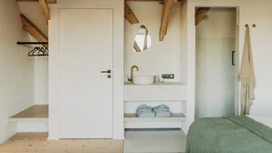 Un dormitorio con techo de madera, una puerta blanca, un lavamanos blanco con grifo dorado, un espejo y una colcha verde.