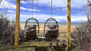 Een houten pergola met twee hangschommels boven een strand.