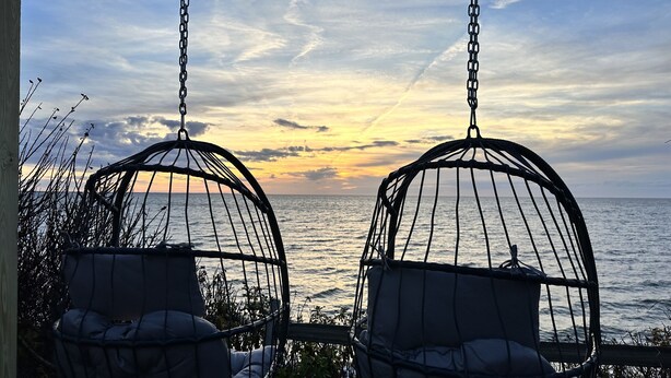 Twee rieten hangstoelen gericht op een zonsondergang boven de oceaan.