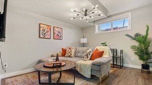 A living room with a grey sofa, a coffee table, a lamp, and a large plant. - Suburban Restful Retreat 1BD 1BA, WiFi, Laundry (Calgary)