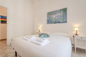 A neatly made bed with white linens and towels, a painting of a landscape, and two bedside tables with lamps. - ToMo Apartment St. Peter's (Roma)
