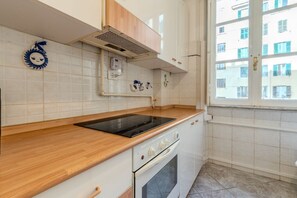 Une cuisine dotée d’un plan de travail en bois, d’une cuisinière encastrée et d’une fenêtre donnant sur des immeubles.