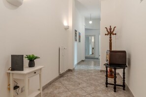 Un couloir avec une console blanche, une plante en pot, un porte-manteau et un radiateur.