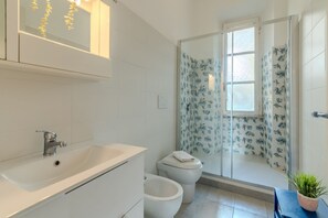 A modern bathroom with a white sink, two toilets, a glass shower enclosure with floral curtains, and a small potted plant. - ToMo Apartment St. Peter's (Roma)