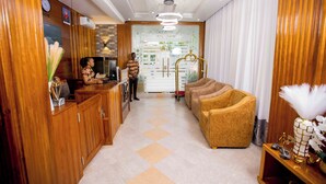 A hotel lobby with wooden paneling, a reception desk, a seating area with sofas, and a decorative vase with white feathers. - HADJENS HOTEL (Mwanza)