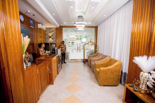 Un hall d’hôtel avec des boiseries, un comptoir d’accueil, un espace salon avec des canapés et un vase décoratif orné de plumes blanches.