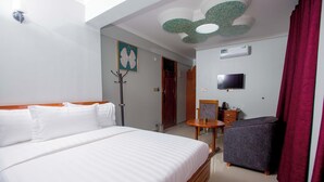 A hotel room with a large bed, a small table, a chair, a TV, and a ceiling fan. - HADJENS HOTEL (Mwanza)