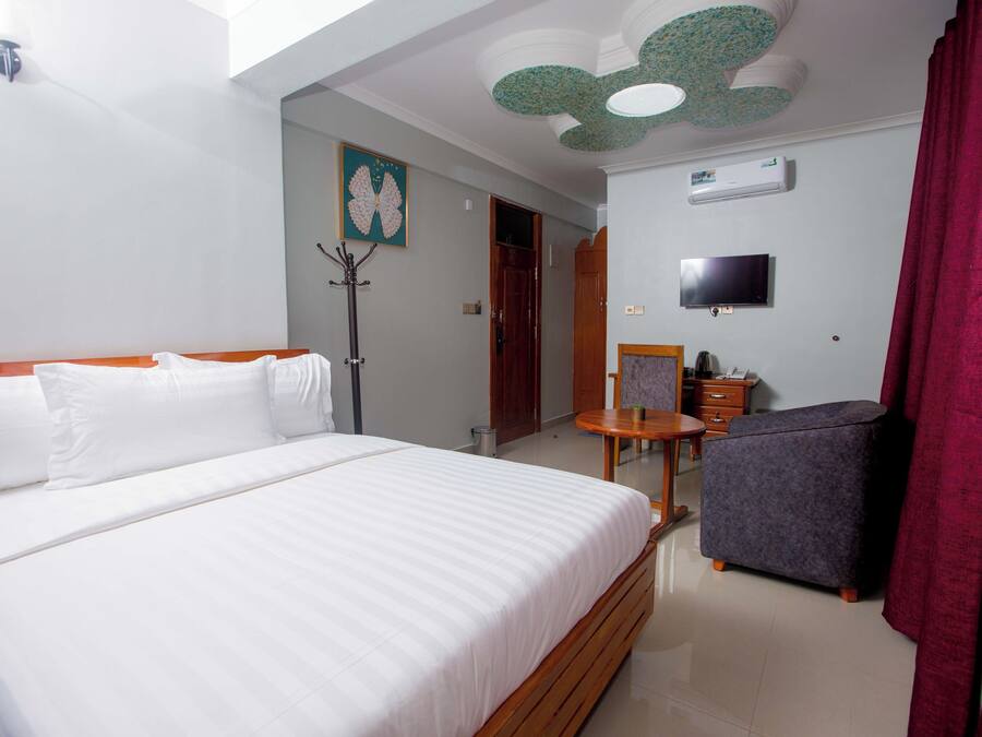 A hotel room with a large bed, a small table, a chair, a TV, and a ceiling fan.