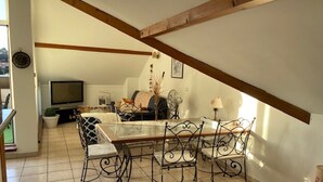 A dining area with a table and chairs, a television in the background, and a staircase leading to an upper level. - Bel appartement duplex, terrasse , 2 min du lac ,4pers (Sévrier)