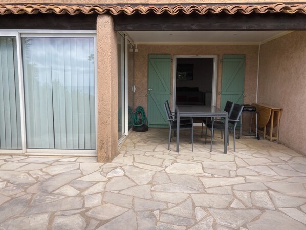 A patio with a table and chairs, a sliding glass door, and a green door leading to an interior room. - Appt 4 Pers, Entrée Privative, Jardinet, vue mer , 1 Place Parking Privative (Roquebrune-sur-Argens)