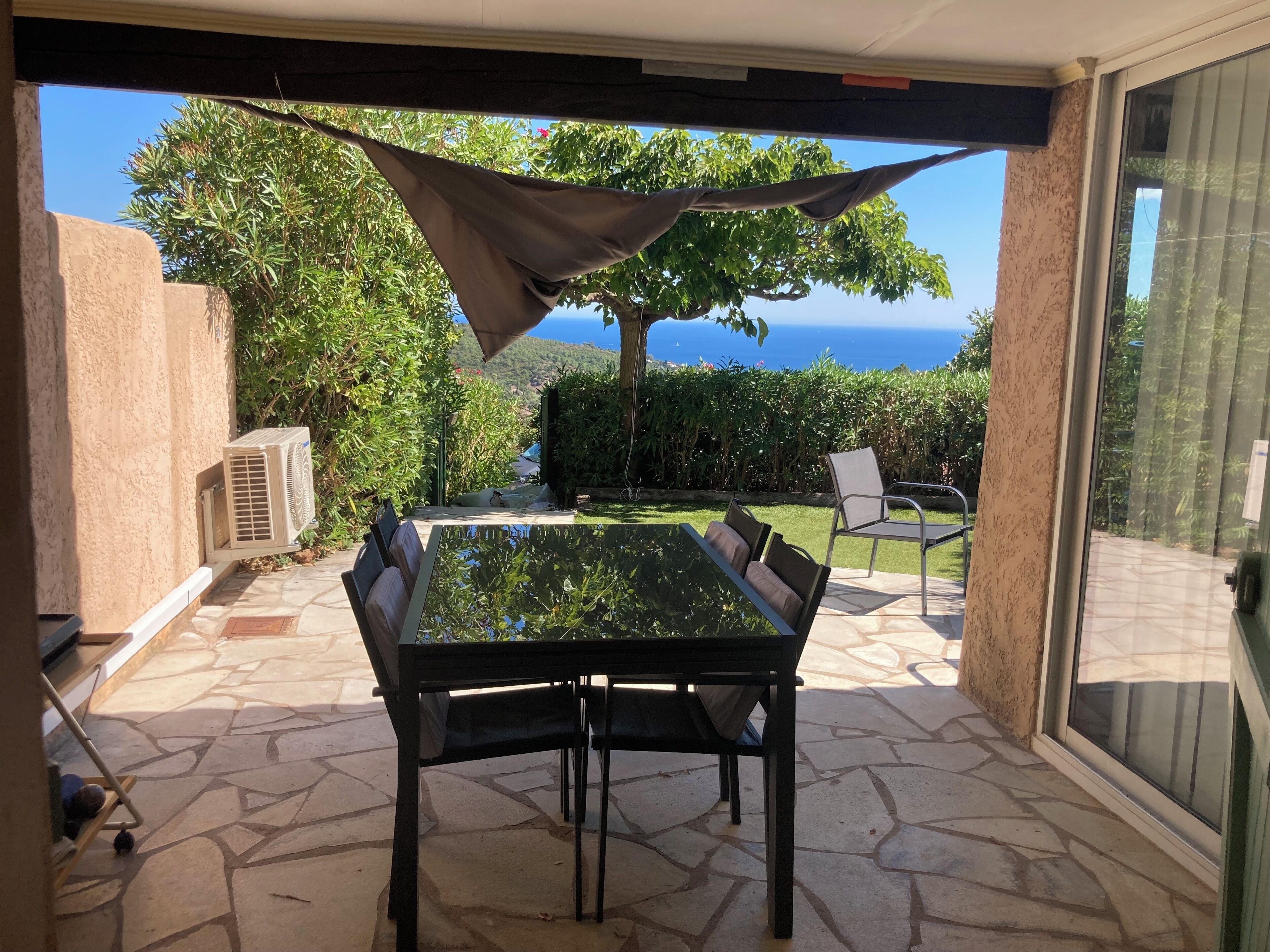 A patio with a table and chairs, a hanging shade, and a view of the sea.